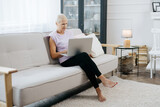 elderly woman with a laptop sitting on the sofa in her living room.