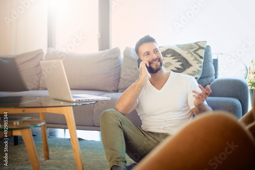 Man sitting on the floor at home and talking on his mobile phone