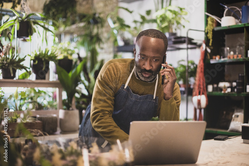 Plant shop owner using a laptop computer and smartphone in store