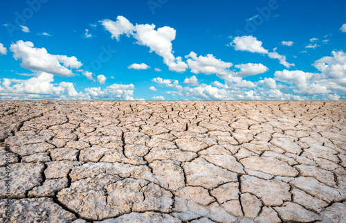 The land that is barren and cracked from the hot sun in the summer, with the bright light of the sun as white clouds and blue sky background