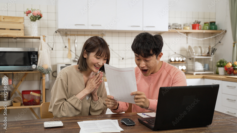 cheerful Asian couple happy while making budget plan at home. man screams with raised fist as woman applauds and pointing at computer, happy about being able to afford dream house cheerful Asian couple happy while making budget plan at home. man screams with raised fist as woman applauds and pointing at computer, happy about being able to afford dream house