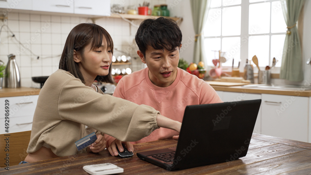 smiling asian husband and wife pointing at computer while discussing what to buy on the internet at home. they pay online with a credit card smiling asian husband and wife pointing at computer while discussing what to buy on the internet at home. they pay online with a credit card
