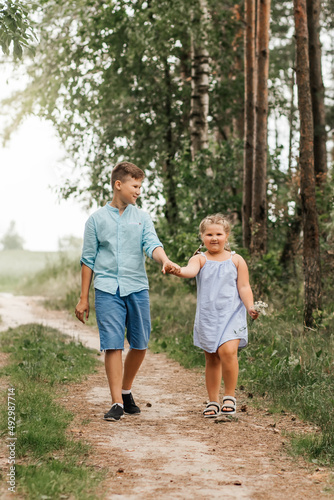 Brother and sister walking together on path in the countryside in summer