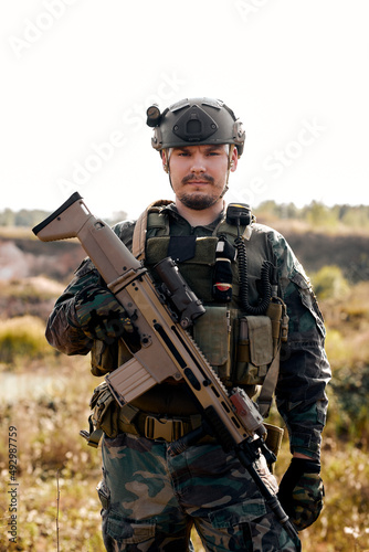 confident military man in uniform holding rifle, posing at camera outdoors. Anti-terror concept. Caucasian european male looking at camera, alone. army soldier ready to shoot with assault rifle