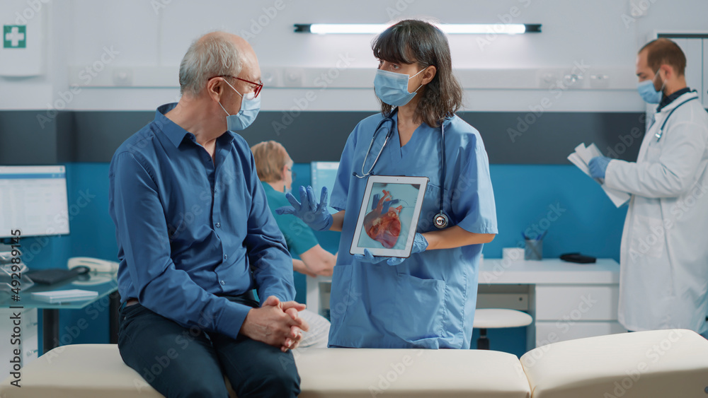 Obraz premium Nurse and elder patient looking at cardiology illustration on digital tablet during coronavirus pandemic. Woman and man analyzing cardiovascular system and heart condition on screen.