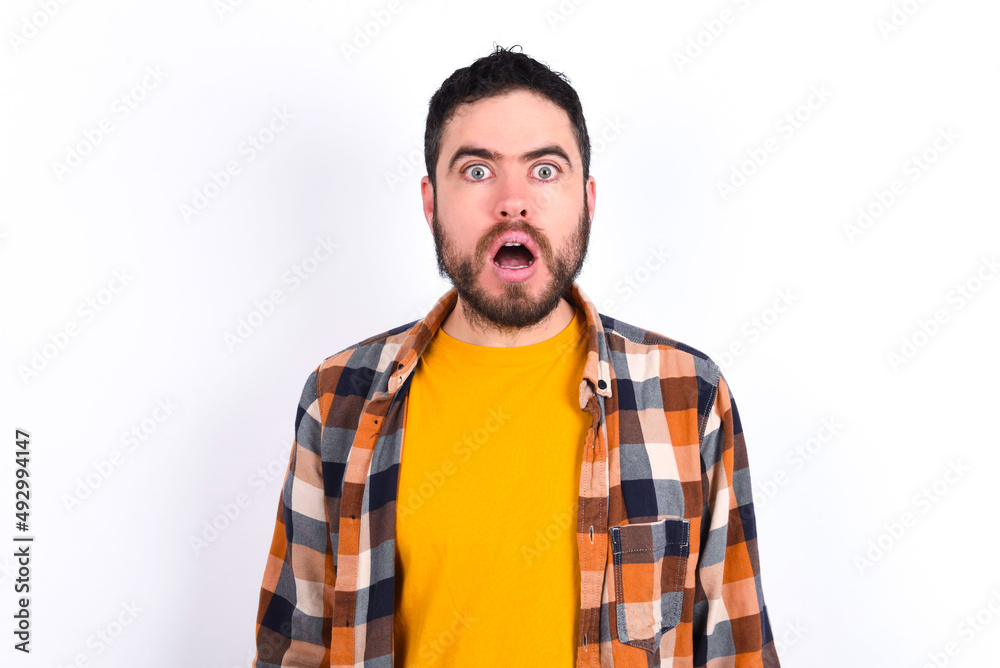 young caucasian man wearing plaid shirt over white background having stunned and shocked look, with mouth open and jaw dropped exclaiming: Wow, I can't believe this. Surprise and shock young caucasian man wearing plaid shirt over white background having stunned and shocked look, with mouth open and jaw dropped exclaiming: Wow, I can't believe this. Surprise and shock