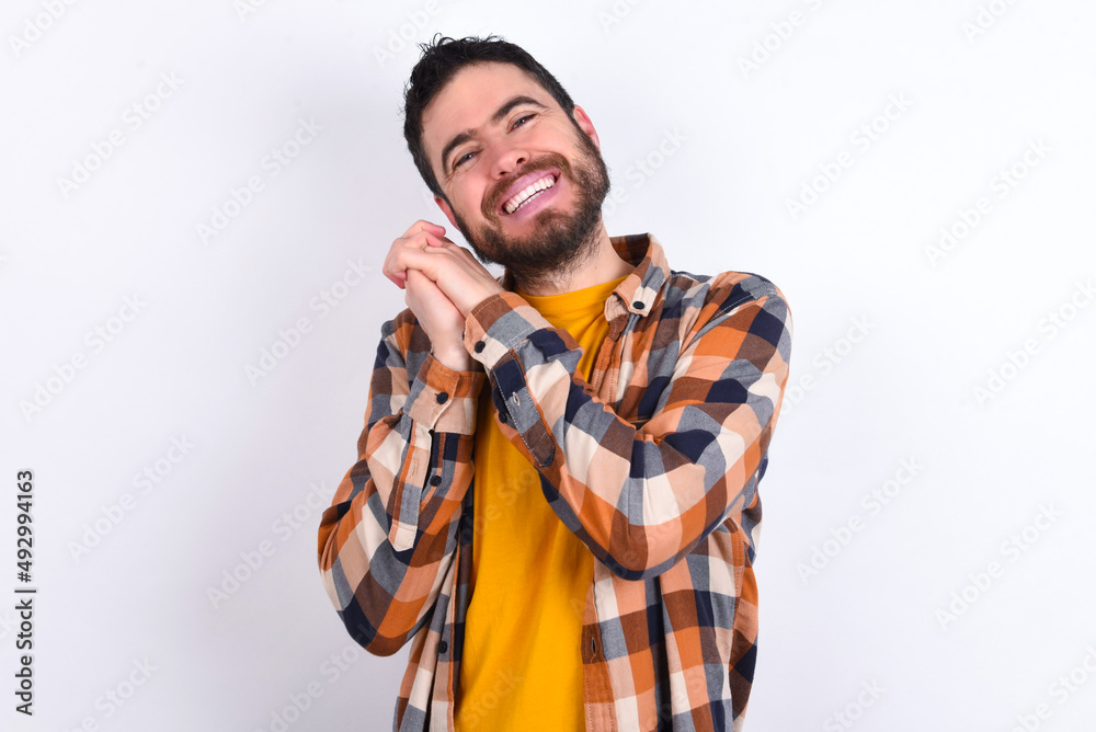 Dreamy young caucasian man wearing plaid shirt over white background with pleasant expression, closes eyes, keeps hands crossed near face, thinks about something pleasant Dreamy young caucasian man wearing plaid shirt over white background with pleasant expression, closes eyes, keeps hands crossed near face, thinks about something pleasant