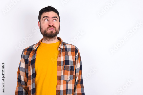 young caucasian man wearing plaid shirt over white background, looks pensively aside, plans actions after university, imagines what to do Thinks over about new project.