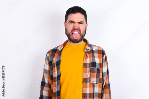 Body language. Disgusted stressed out young caucasian man wearing plaid shirt over white background, frowning face, demonstrating aversion to something.
