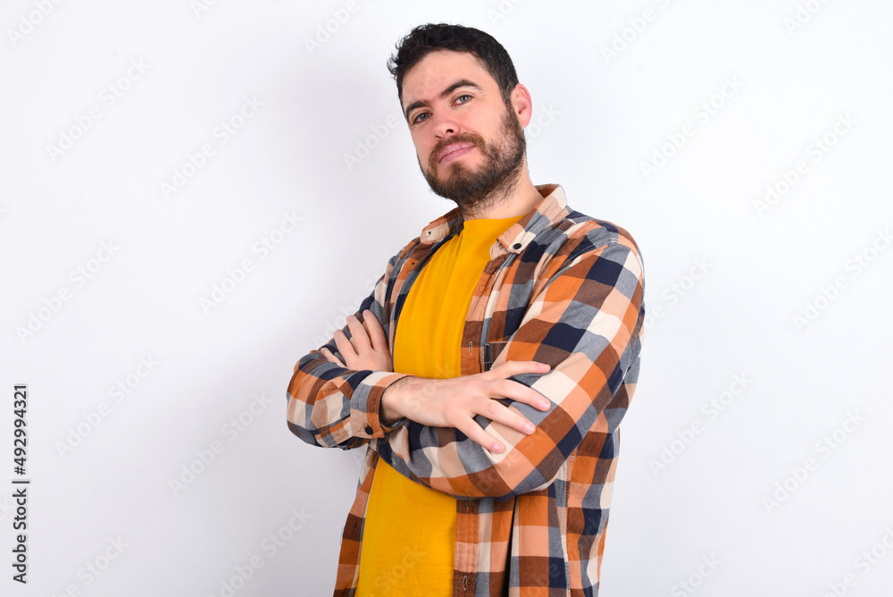 Waist up shot of  self confident young caucasian man wearing plaid shirt over white background has broad smile, crosses arms, happy to meet with colleagues.