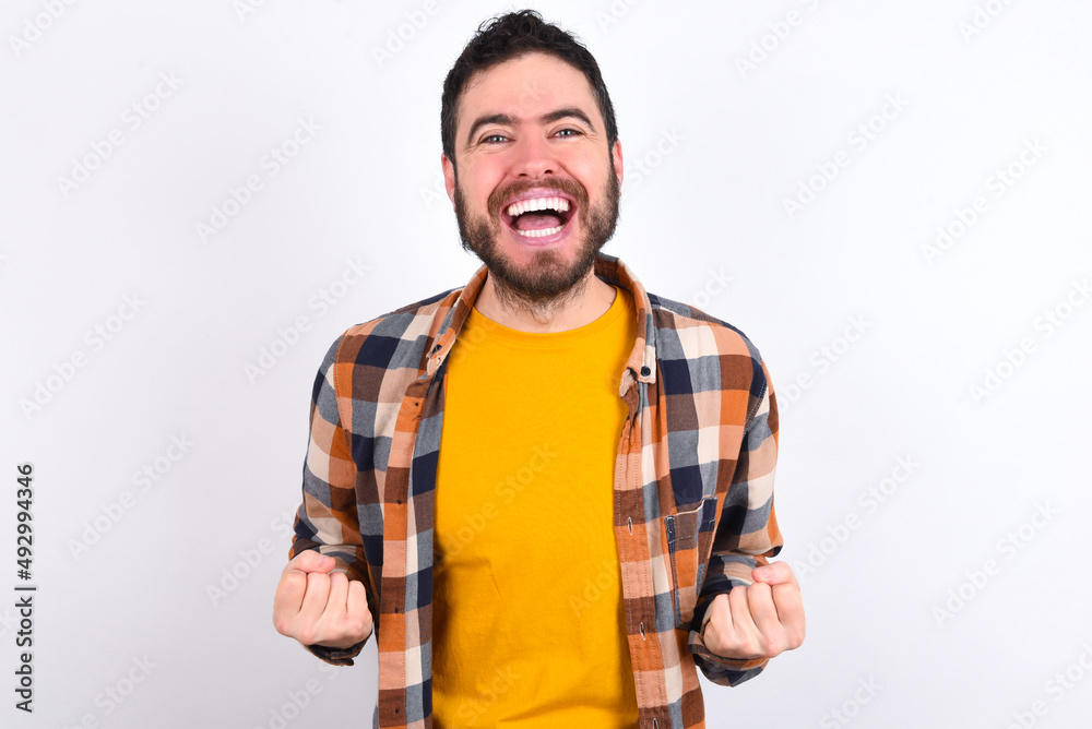 young caucasian man wearing plaid shirt over white background raising fists up screaming with joy being happy to achieve goals. young caucasian man wearing plaid shirt over white background raising fists up screaming with joy being happy to achieve goals.