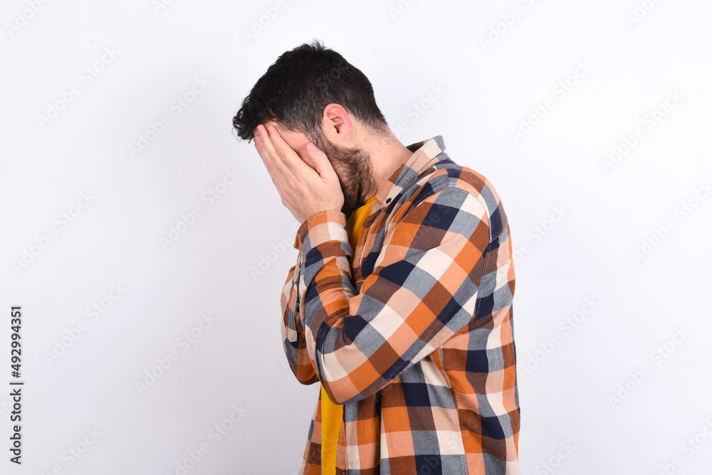 Sad young caucasian man wearing plaid shirt over white background covering face with hands and crying. Sad young caucasian man wearing plaid shirt over white background covering face with hands and crying.