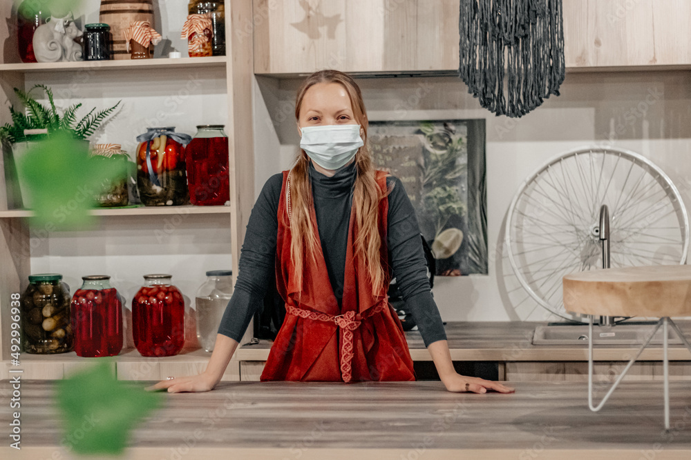 A girl in a medical mask stands at a large wooden table.