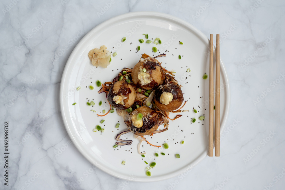 A plate of takoyaki with chopsticks over a marble table