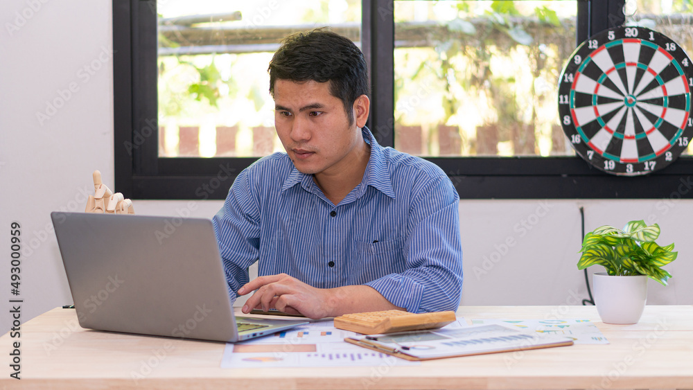 Fototapeta premium Handsome, smart Asian businessman working from home in the office. Computing reports. Paperwork financiers. use a laptop and a calculator
