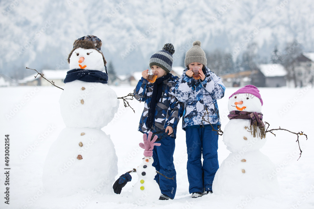 Family with children, building snowman in the park in little village in Austria