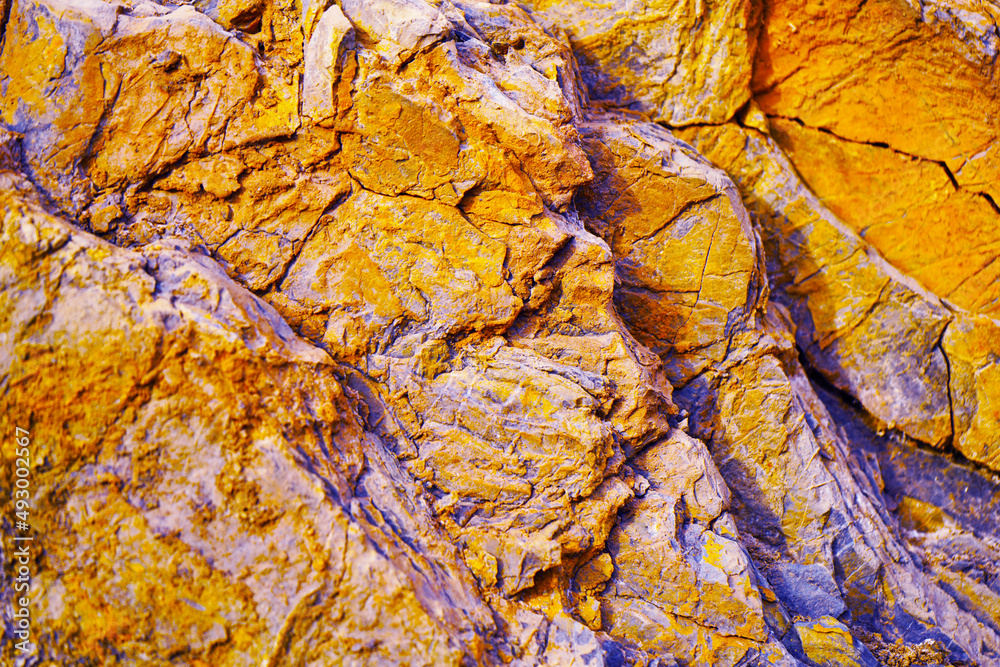 Abstract orange yellow blue background. Colorful rock texture. Cracked layered mountain surface. Close-up. Grungy stone background with space for design.