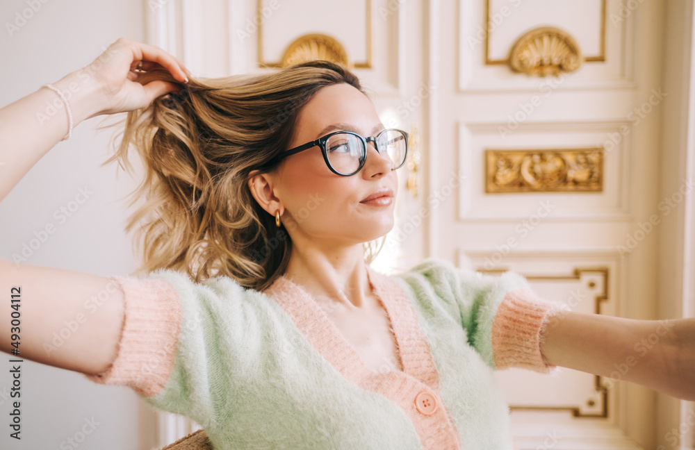 Naklejka premium Portrait of attractive caucasian young woman in eyeglasses sitting on armchair in bright living room near ornamental door.