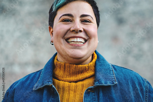 carefree young cheerful androgenic looking person with toothy smile close-up looking at camera - really confident hipster style person with piercing isolated on blurred background - body positives
