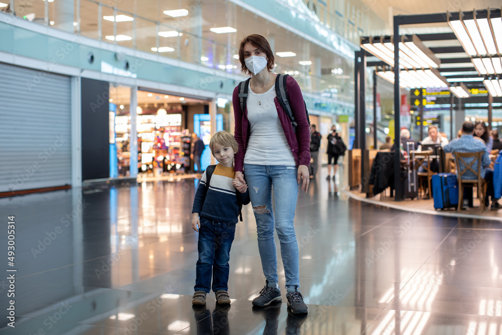 Fototapeta premium Cute baby boy waiting boarding to flight in airport transit hall near departure gate. Active family lifestyle travel by air with children