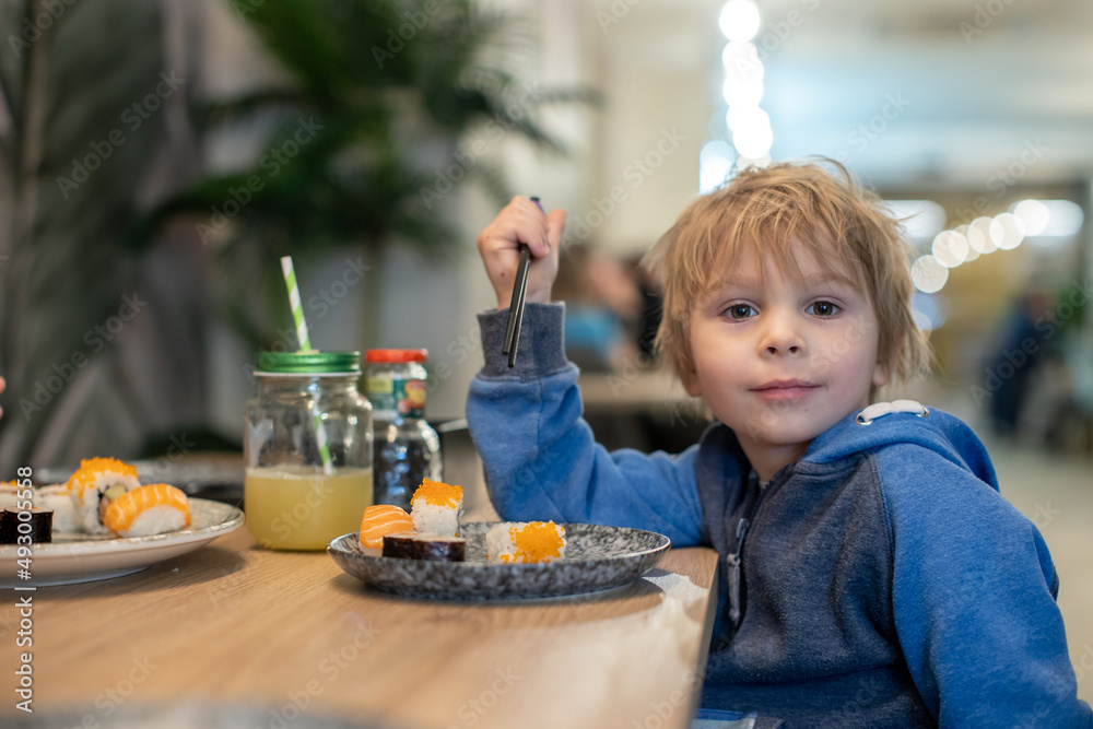 Child, eating japanese sushi and noodles with chopsticks in a restaurant