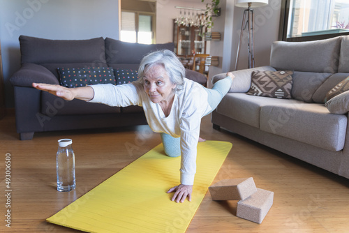 Older caucasian woman in sportswear doing gymnastic exercises on the living room floor with a mat