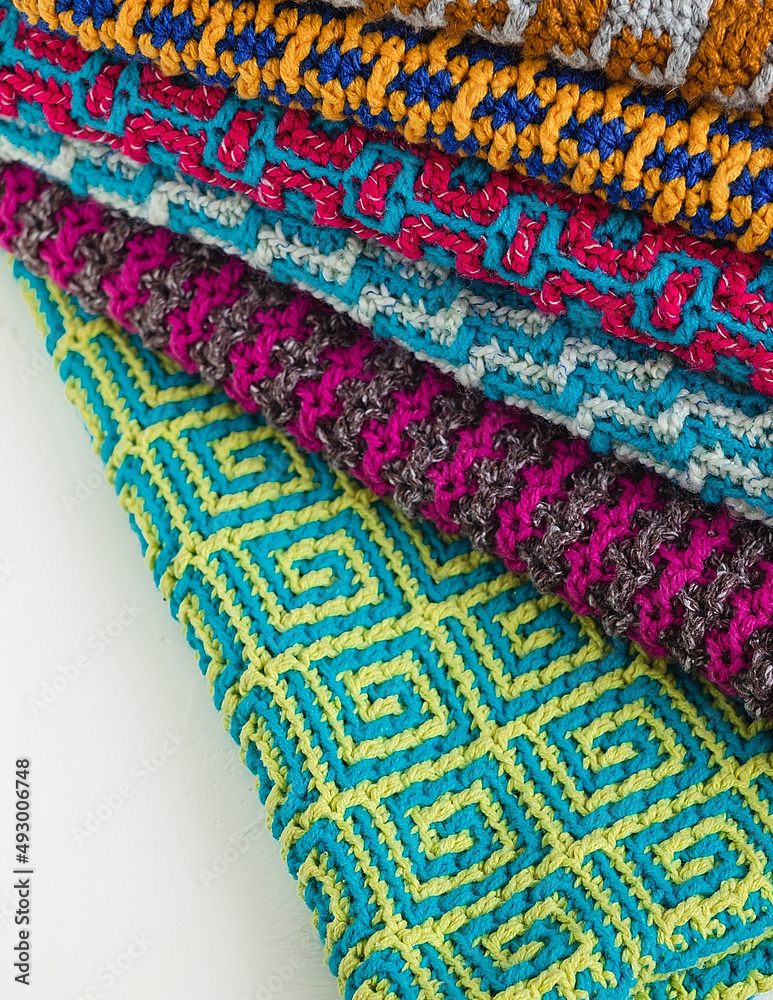 Stack of bright colored crochet fabric with geometric pattern. Colored knitted texture with mosaic technique.