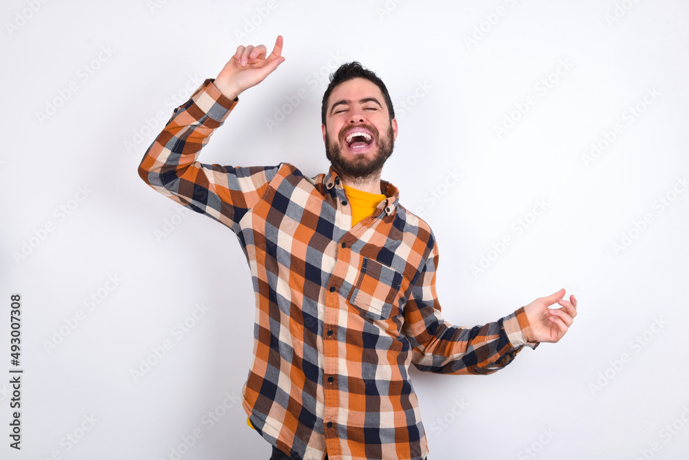 Naklejka premium Photo of upbeat young caucasian man wearing plaid shirt over white background has fun and dances carefree wear being in perfect mood makes movements. Spends free time on disco party