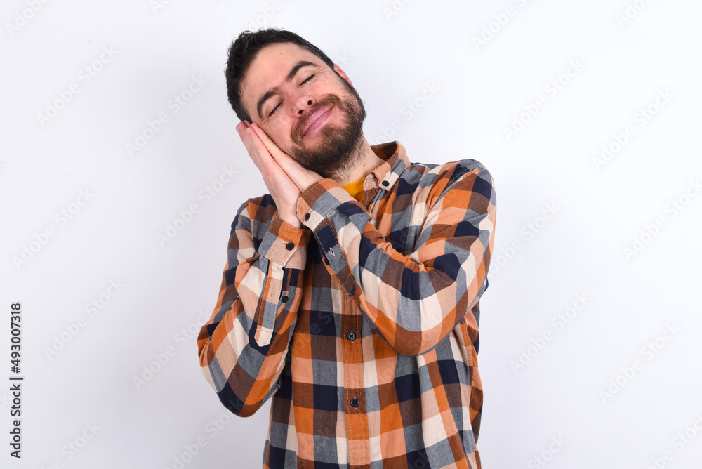 young caucasian man wearing plaid shirt over white background leans on pressed palms closes eyes and has pleasant smile dreams about something young caucasian man wearing plaid shirt over white background leans on pressed palms closes eyes and has pleasant smile dreams about something