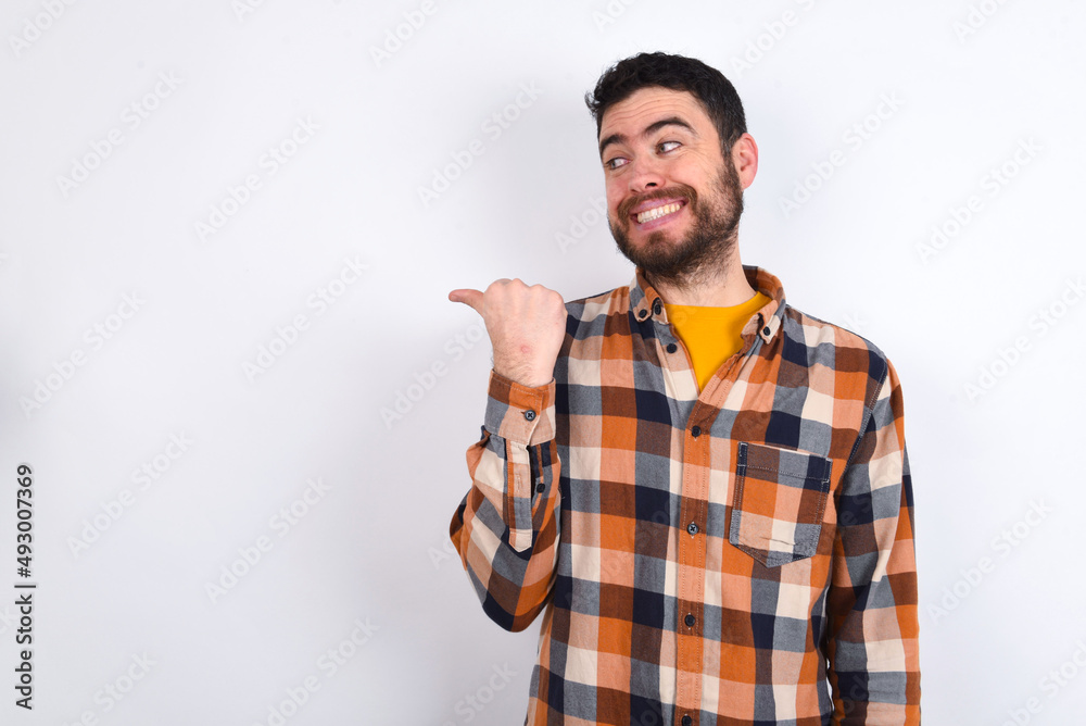 young caucasian man wearing plaid shirt over white background points away and gives advice demonstrates advertisement