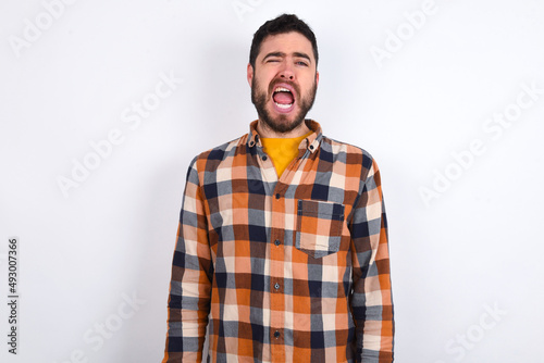 young caucasian man wearing plaid shirt over white background yawns with opened mouth stands. Daily morning routine