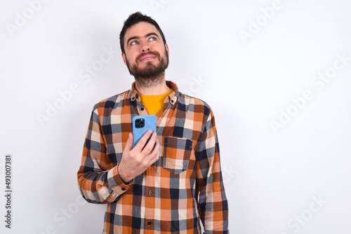 young caucasian man wearing plaid shirt over white background holds mobile phone uses high speed internet and social networks has online communication. Modern technologies concept