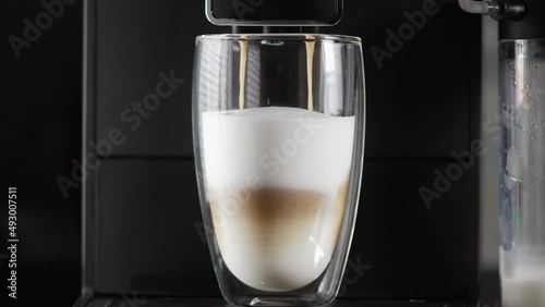 Making cafe latte or moccha coffee in a glass in a close up side view on the beverage with frothed milk over black photo