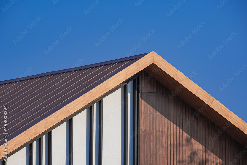 Sunlight on surface of vintage wooden gable roof with battens decoration against blue sky background in perspective side view