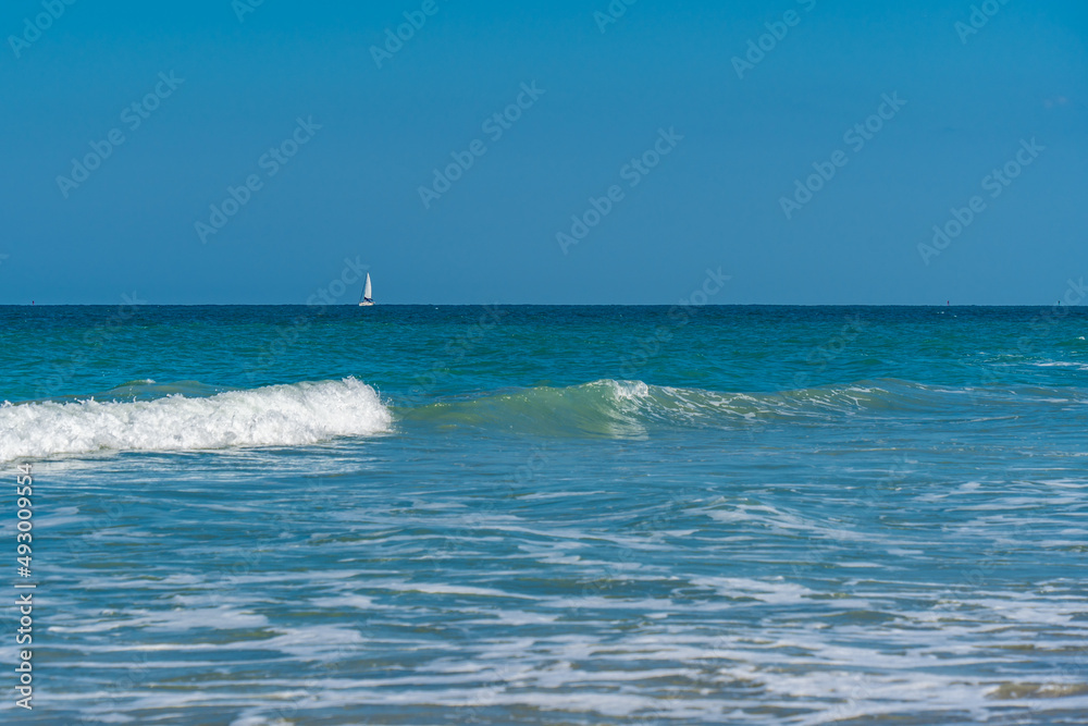 Waves Breaking with Sailboat in Distance