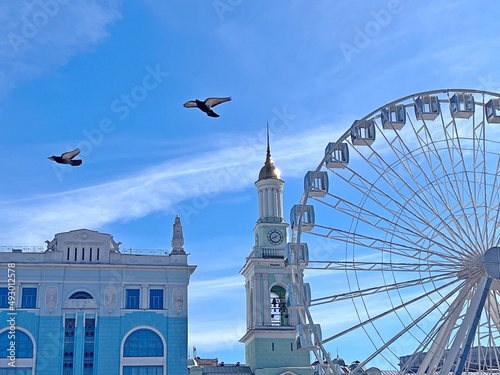 Kyiv city capital of Ukraine beautiful cityscape. Kiev old town peaceful scenic view.  Flying doves fly over the Ferris wheel. Clear sky at sunny day above Kontraktova square. photo