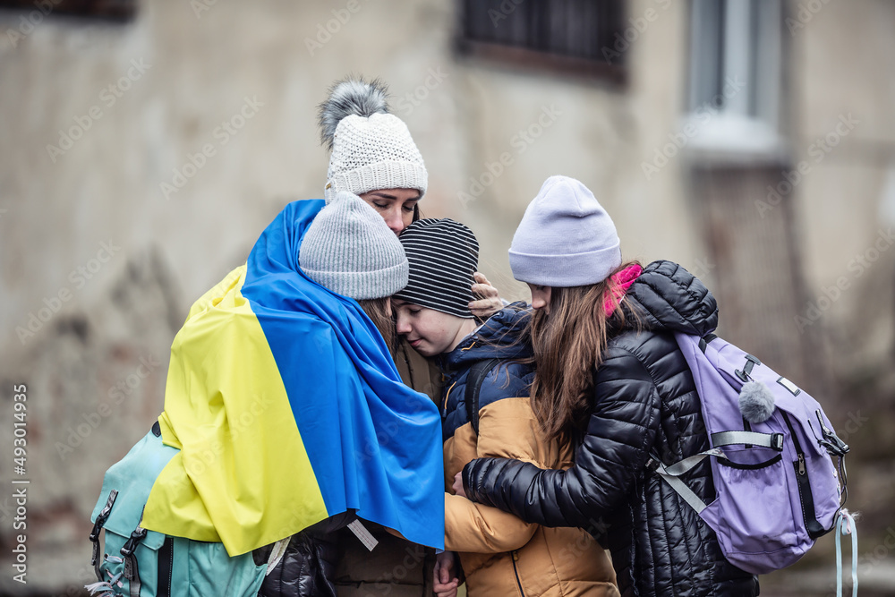 Ukrainian woman holds her three children all sad from being forced to flee their home country and become refugees - obrazy, fototapety, plakaty 