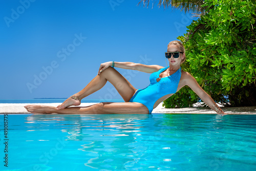 Sexy woman in bikini at Maldives tropical sand beach. Young glamour model in swimsuit near the pool. Perfect body bikini model long blonde hair. Bikini fashion. Luxury travel.
