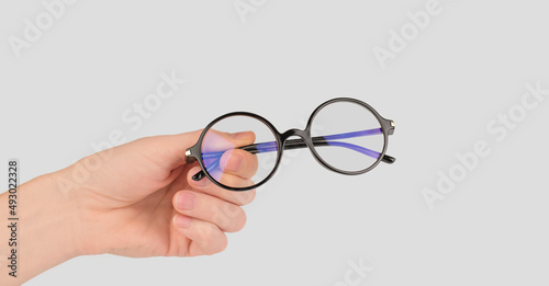Round stylish glasses for vision in a male hand on a gray background, copy space