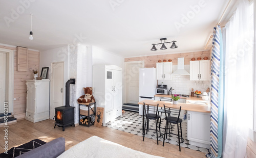 Fototapeta Naklejka Na Ścianę i Meble -  Interior of a bright studio room with a Scandinavian style fireplace in a private house, where the living room is combined with kitchen. in a country house