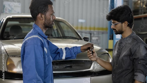 Mechanic giving key by greeting or handshaking customer after car servicing at garage - concept of timely customer service, car maintenance and deal agreemnet. photo