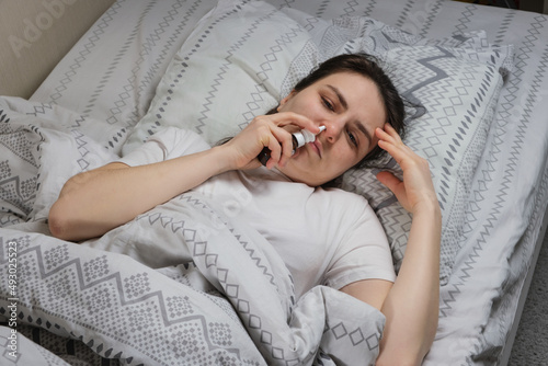 A woman with rhinitis squeaks a saline solution or vasoconstrictor drops into the nose lying in bed, top view. photo