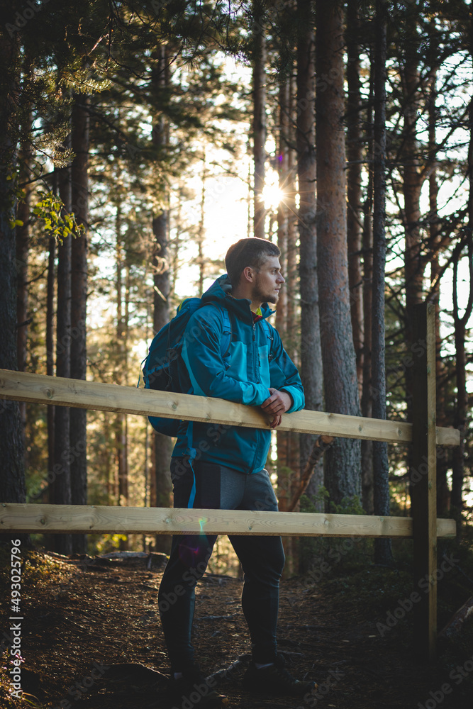 Fototapeta premium Active and exploring man in sportswear rests leaning against a railing after a hard hike, enjoying the view of the valley during sunset. Sotkamo, Finland