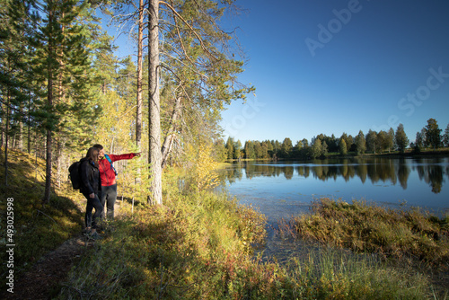 young couple stands on the edge of a lake and the man shows his girlfriend a beautiful spot on the other side. Exploring the Finnish wilderness in Kainuu, Finland. Scandinavian nature
