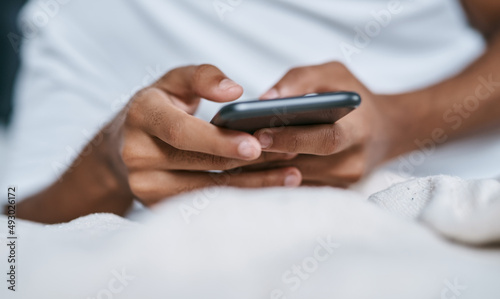 One tap is all it takes to connect. Cropped shot of a man relaxing on his bed and using a smartphone. © Nicholas F/peopleimages.com