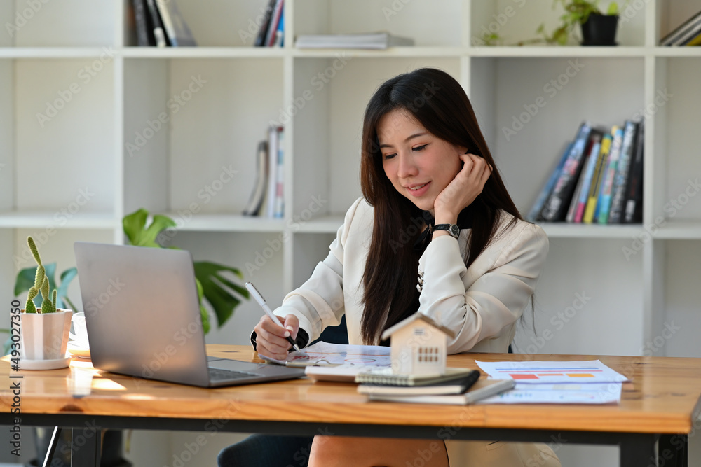 A portrait of a young pretty Asian woman sitting in the office working on a document and laptop, for business, finance and technology concept. A portrait of a young pretty Asian woman sitting in the office working on a document and laptop, for business, finance and technology concept.