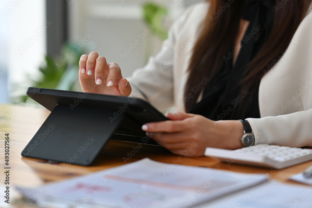 Fototapeta premium Close up woman’s hand using a tablet and calculator in the office and working on data, charts and documents on the table, for finance and technology concept.