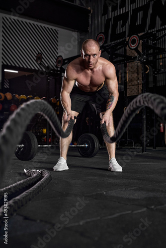 Muscular active man with battle rope doing exercise in functional training fitness gym exercising with battle ropes at gym. caucasian guy working out arms and cardio for cross fit exercises