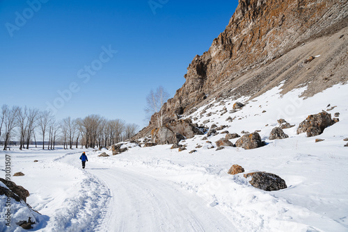 Mountainous terrain in winter. A man walks along a road covered with snow rocks towering over his head.