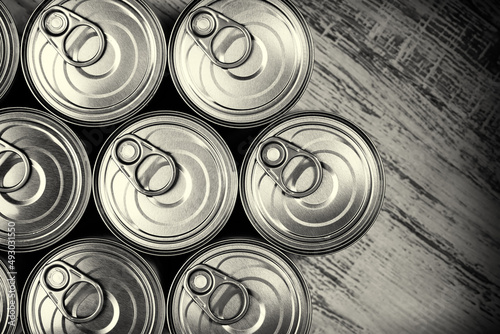 Close up, top down view of a group of tin cans with easy open on a wooden surface. Monochromatic image